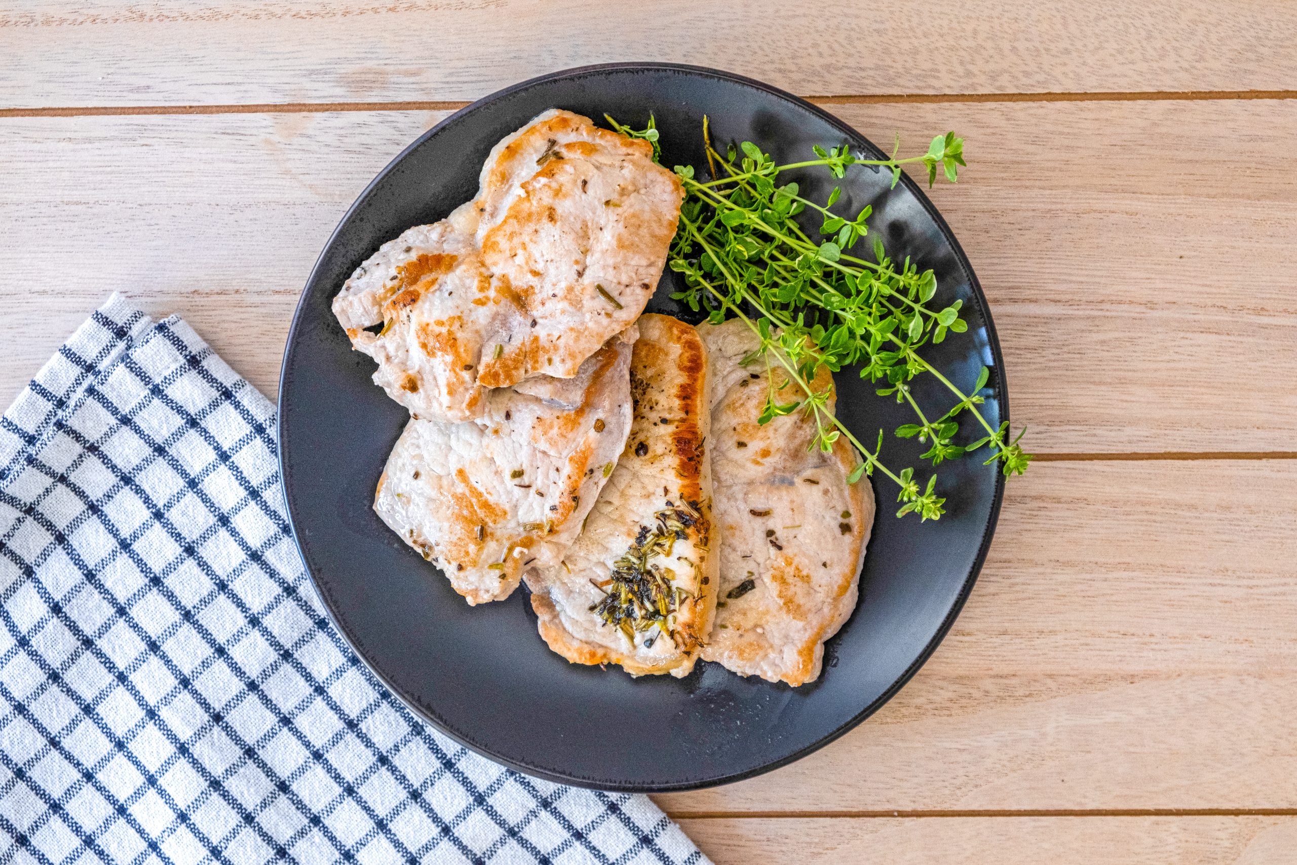 Sliced seasoned pork chops with sprigs of thyme on a dark plate set on a wooden board