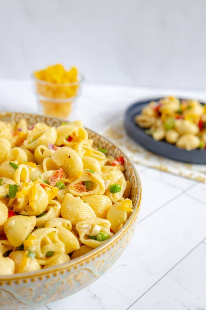 A large bowl filled with cooked elbow noodles tossed with cheese, onion, celery, bell pepper, and peas.