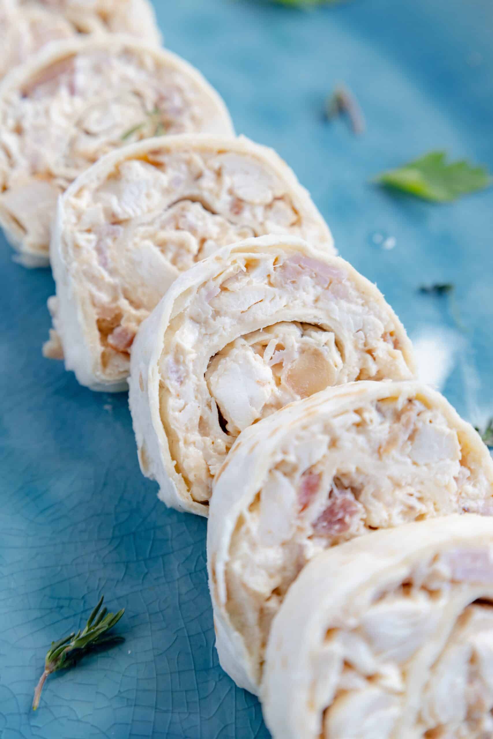 Creamy chicken and bacon tortilla spirals lined up on a blue board