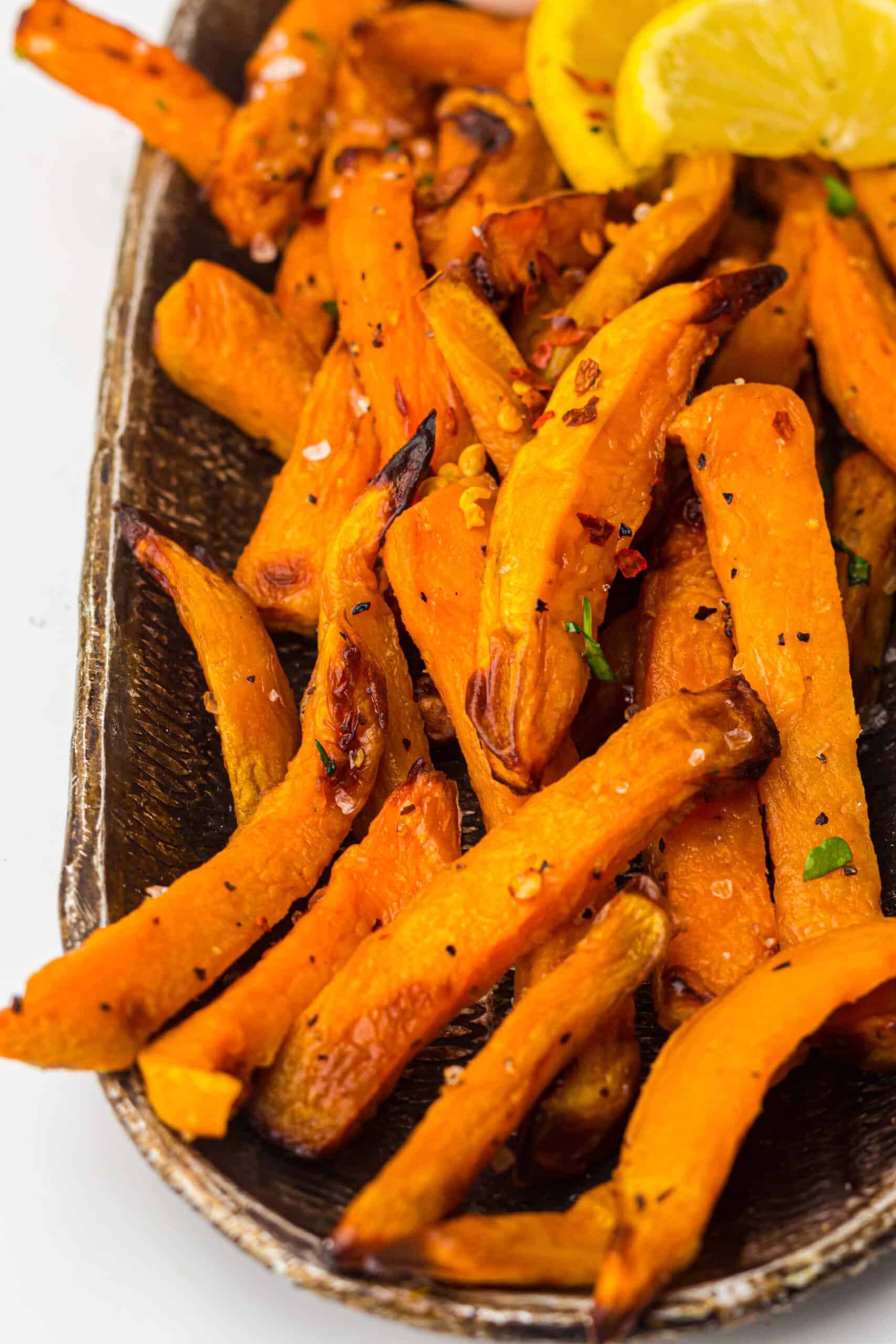 Orange fries with caramelised edges on a dark tray with lemon wedges