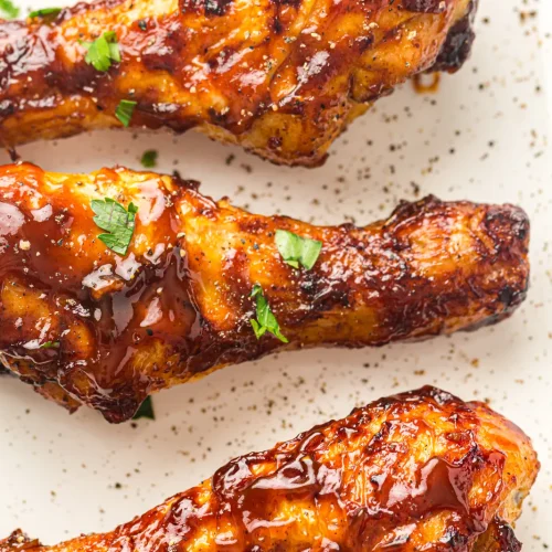 Air fryer BBQ chicken drumsticks glazed in barbecue sauce on a speckled plate