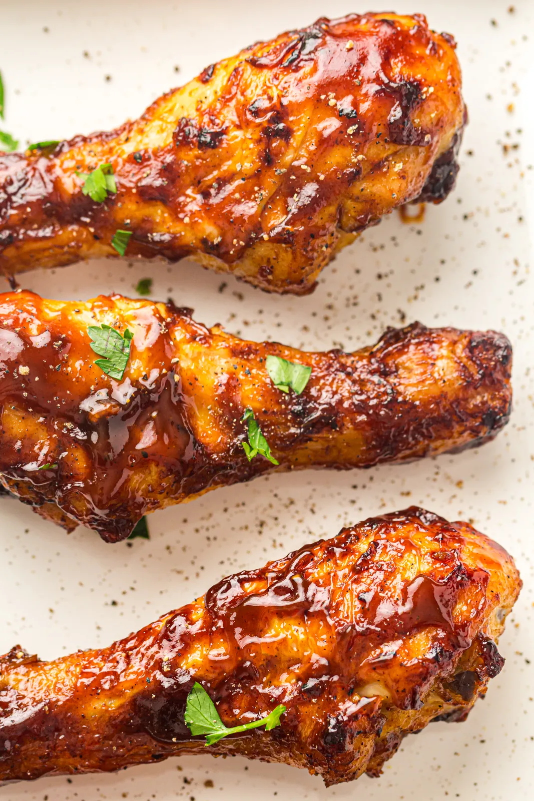 Sticky barbecue glazed drumsticks scattered with parsley on a speckled plate