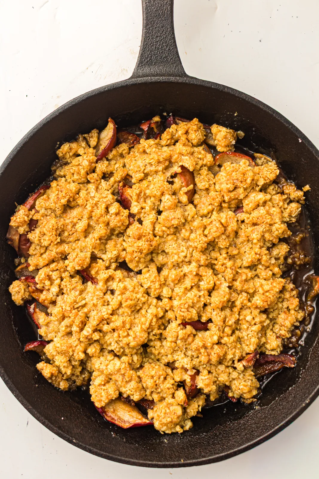 Golden oat crumble over soft cinnamon apples in a black cast iron skillet