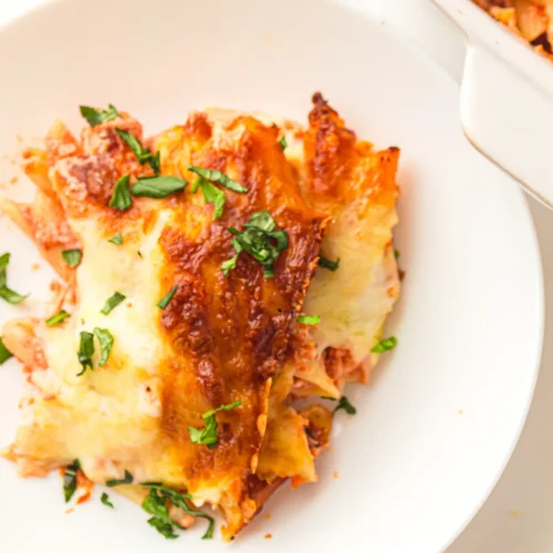 Serving of baked ziti on a white plate topped with fresh basil
