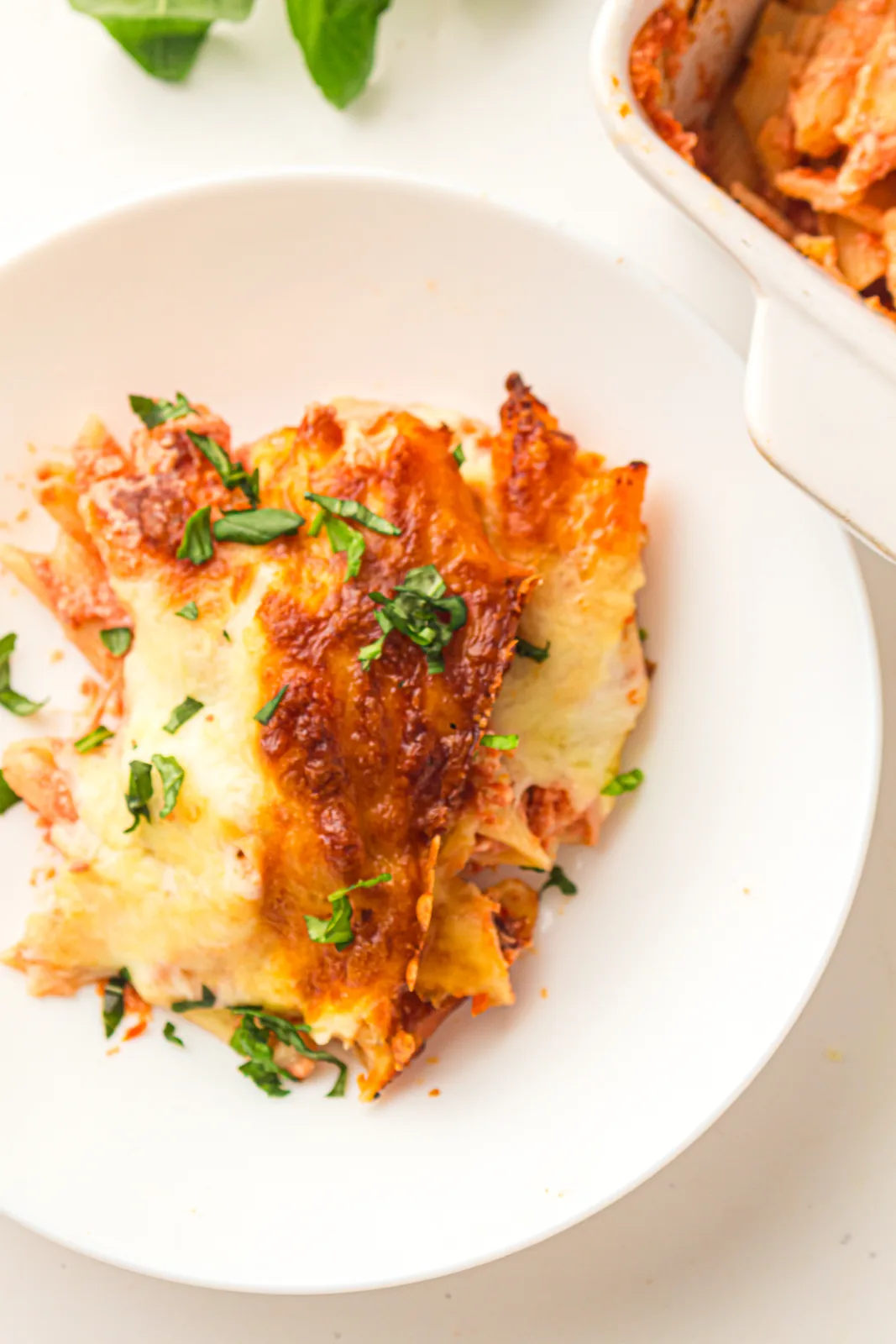 Serving of baked ziti on a white plate topped with fresh basil