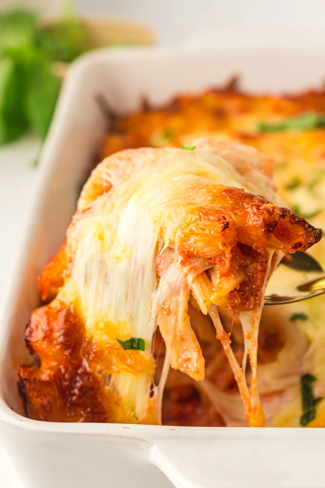Spoon lifting a saucy, cheesy portion from the casserole dish