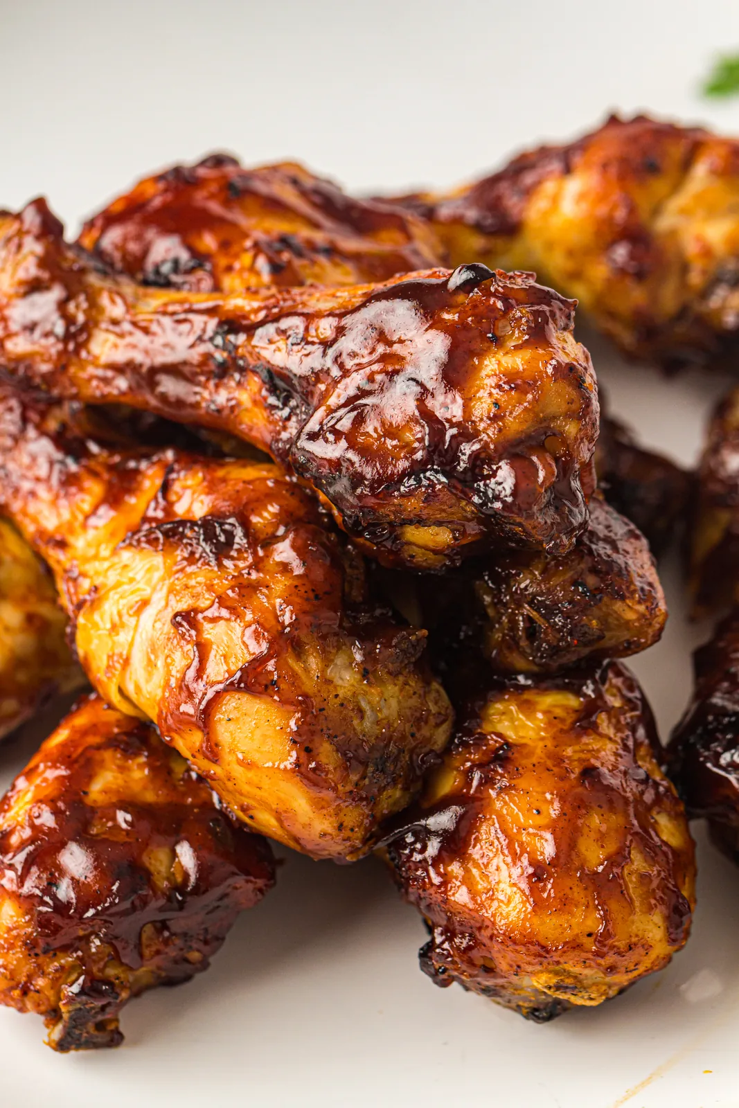 A pile of sticky glazed drumsticks stacked on a white plate