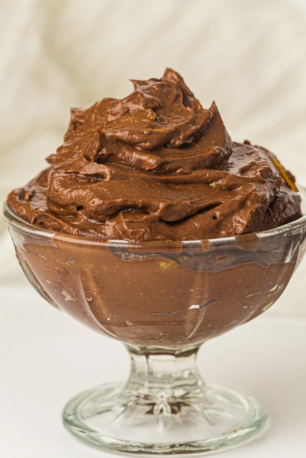 Glossy chocolate mousse piled high in a glass coupe on a white table