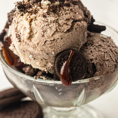 Cookies and cream ice cream in a glass coupe topped with Oreos and chocolate drizzle