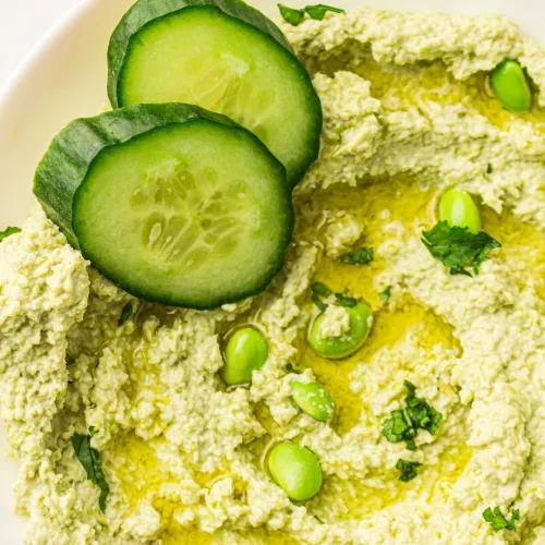 Edamame hummus in a bowl with cucumber slices and olive oil