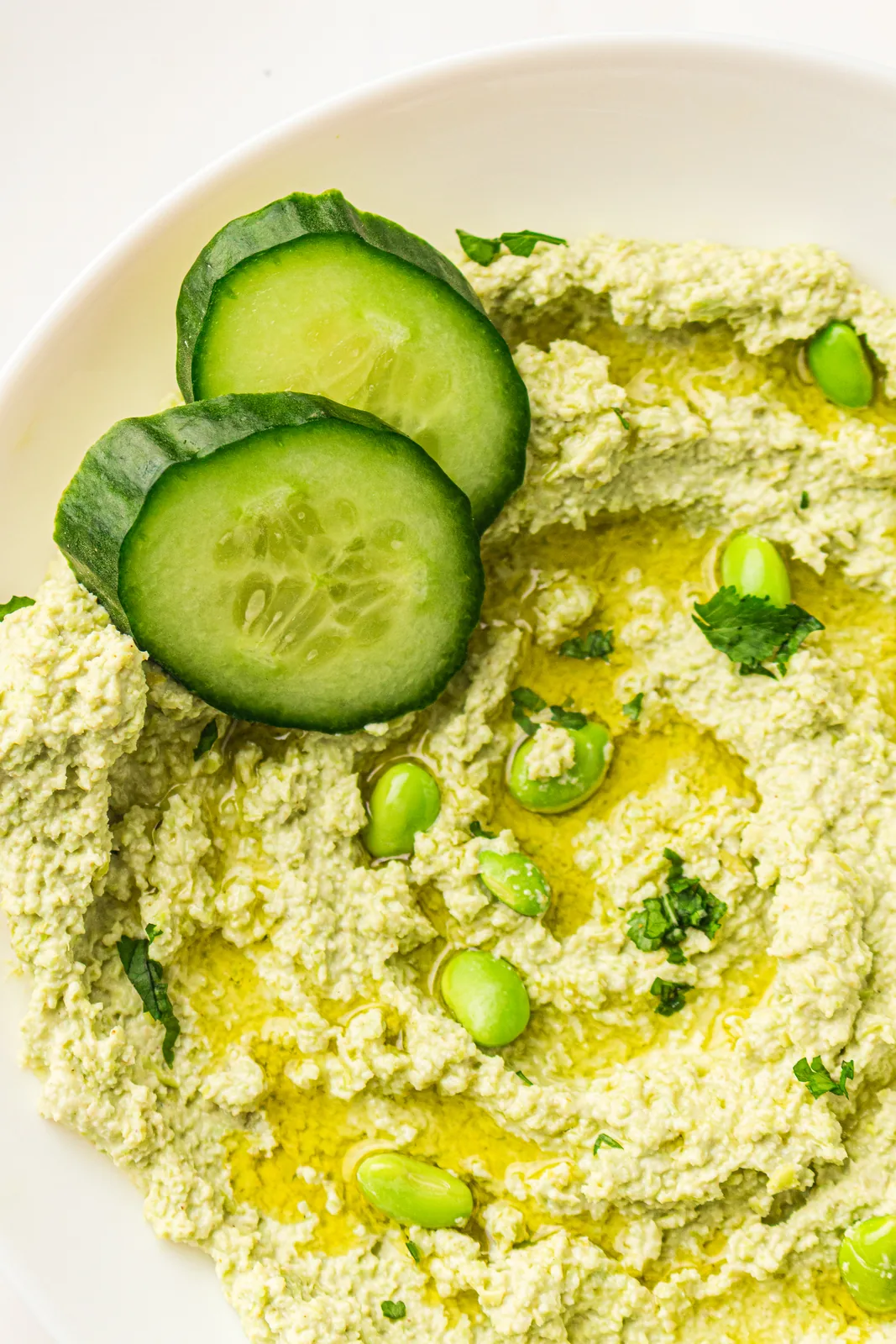 Edamame hummus in a bowl with cucumber slices and olive oil