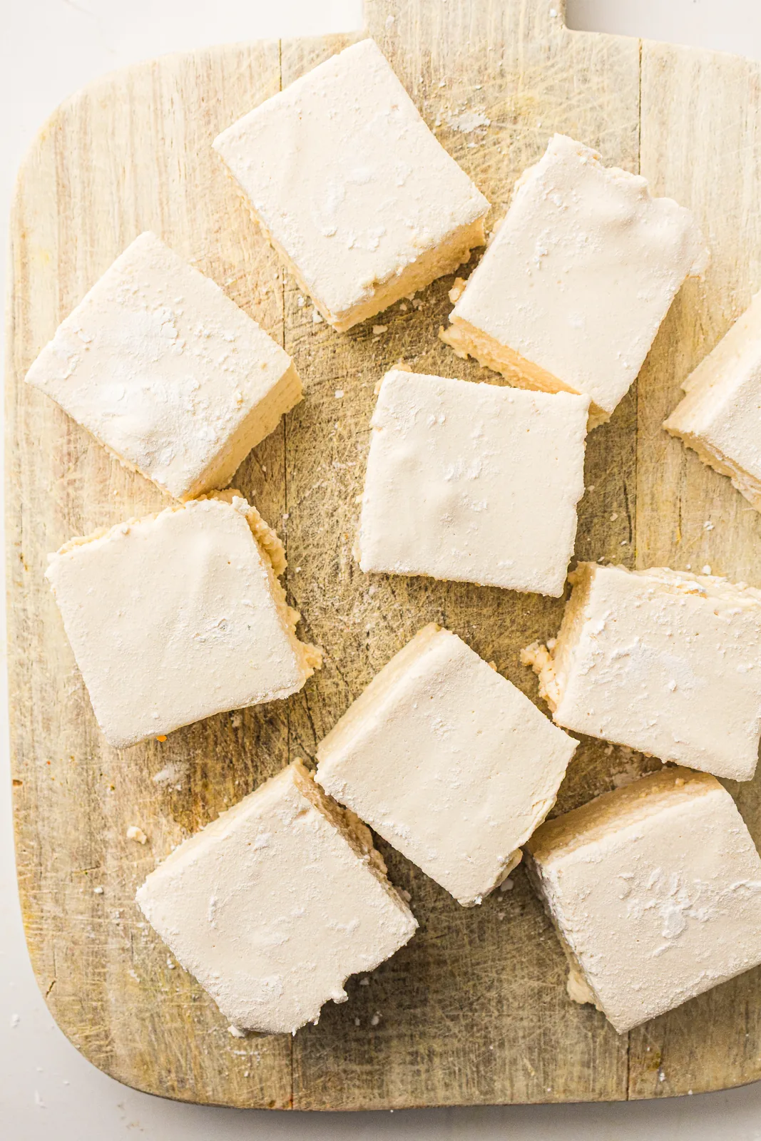 Soft, pillowy vanilla squares stacked on a wooden board