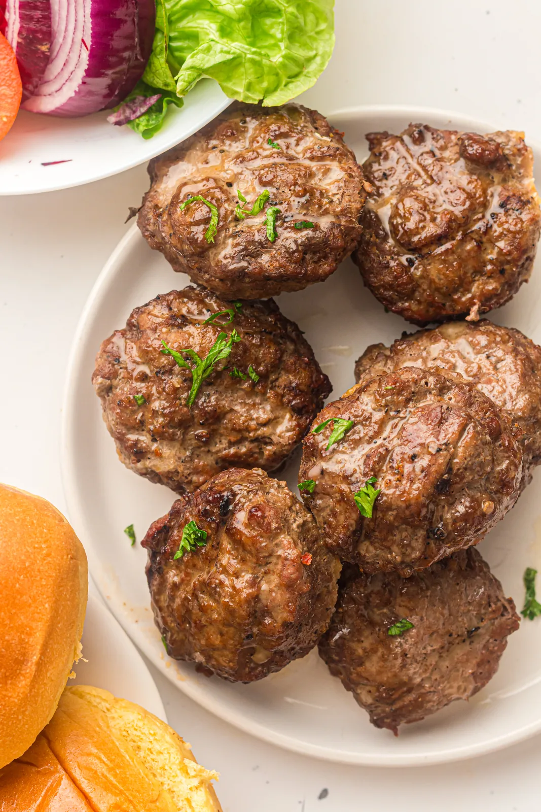 A juicy beef patty on a plate with lettuce, tomato, and red onion