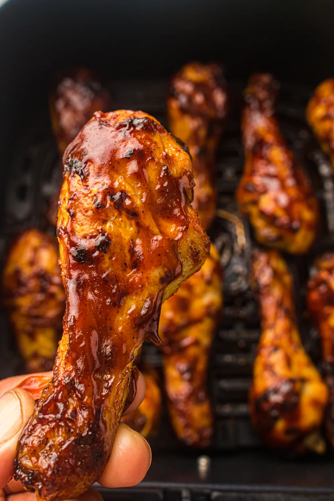 Hand holding a sticky air fryer BBQ chicken drumstick over the basket