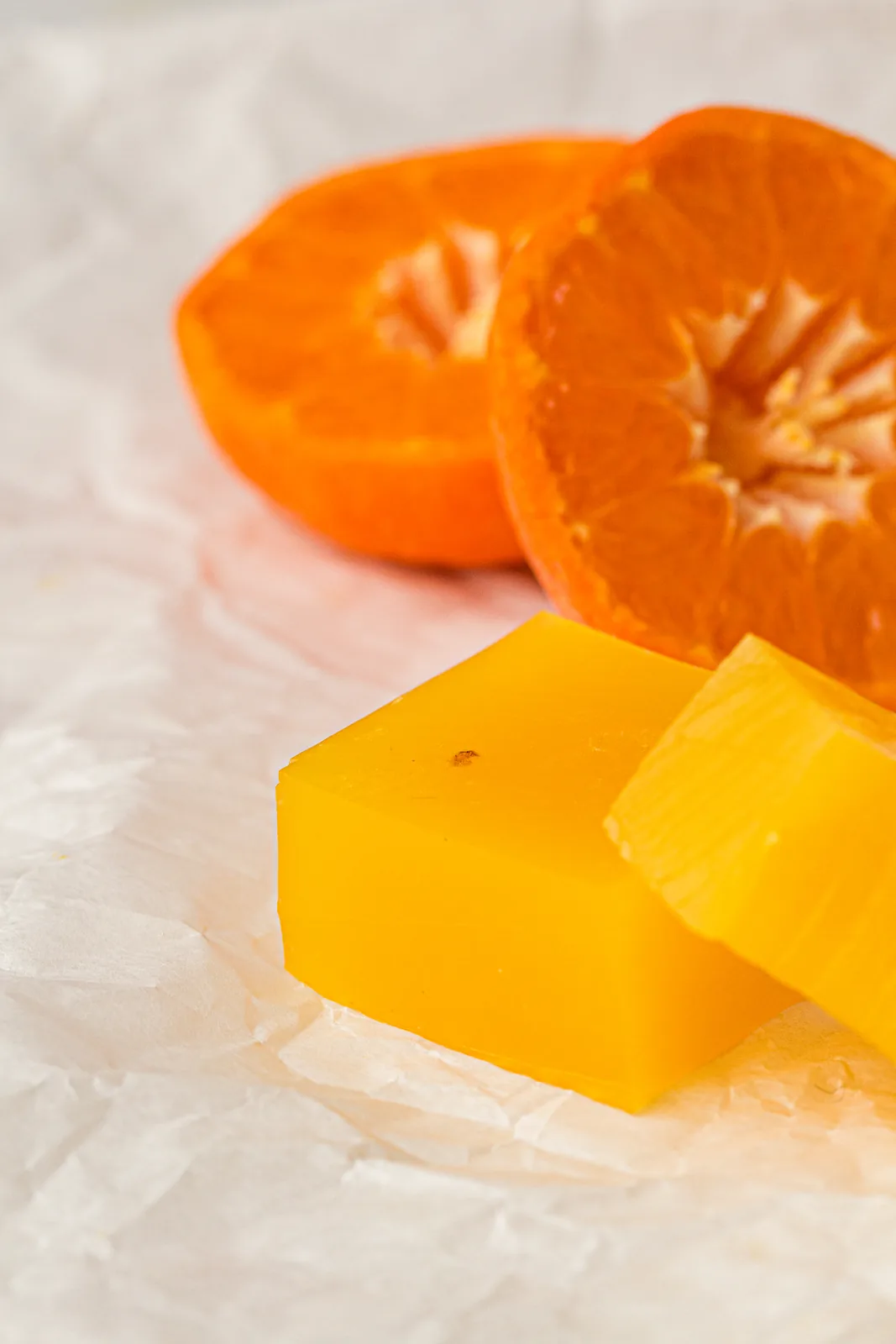 Homemade orange gummies cut into squares beside fresh orange halves