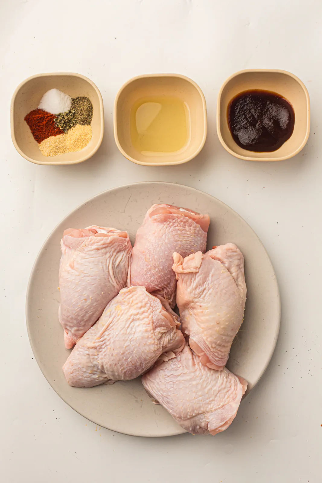Ingredients for smoked chicken thighs including spice rub, oil and BBQ sauce