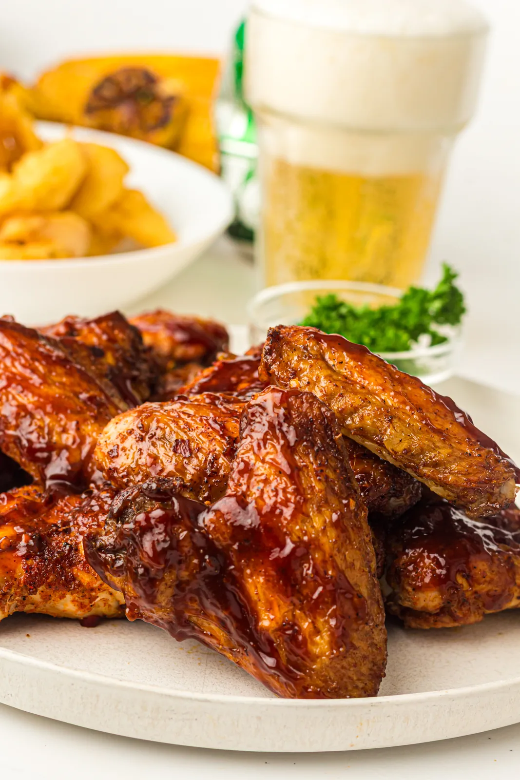 Smoked chicken wings glazed with BBQ sauce on a plate next to a cold beer