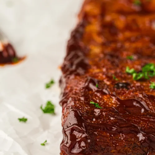 A glossy BBQ-glazed rack of smoked ribs on parchment paper