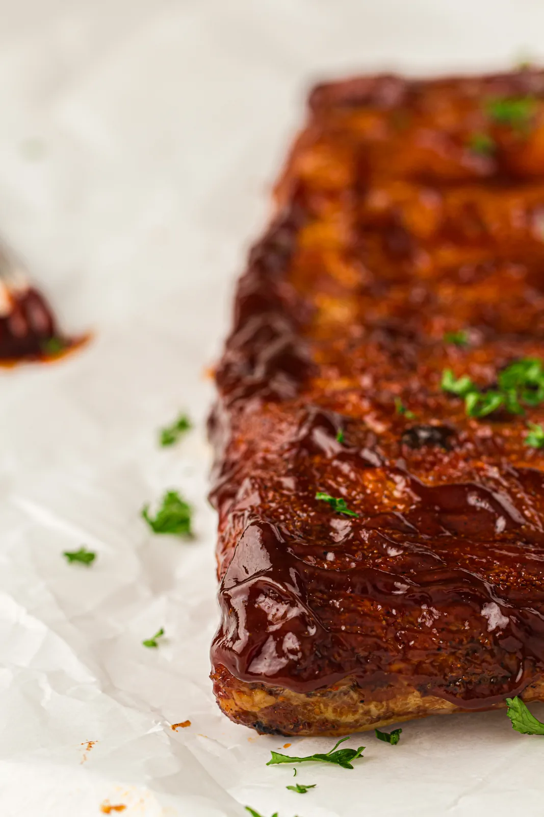 A glossy BBQ-glazed rack of smoked ribs on parchment paper