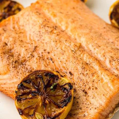 A smoked salmon fillet on a plate with charred lemon halves