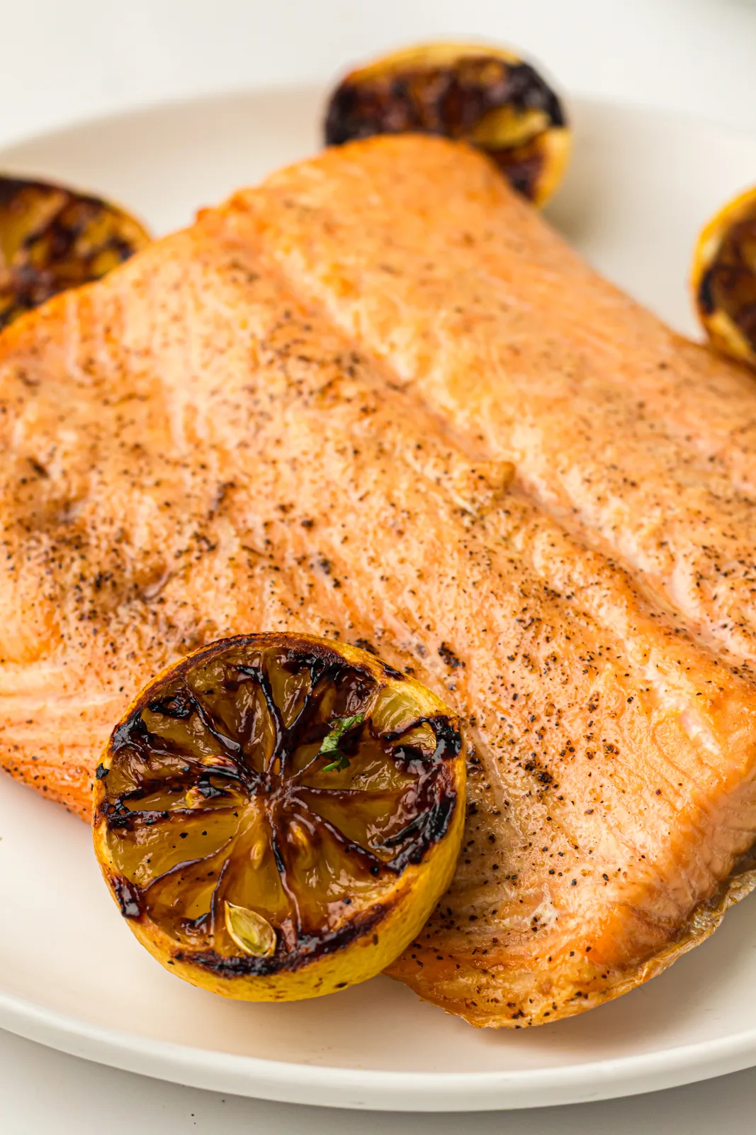 A smoked salmon fillet on a plate with charred lemon halves
