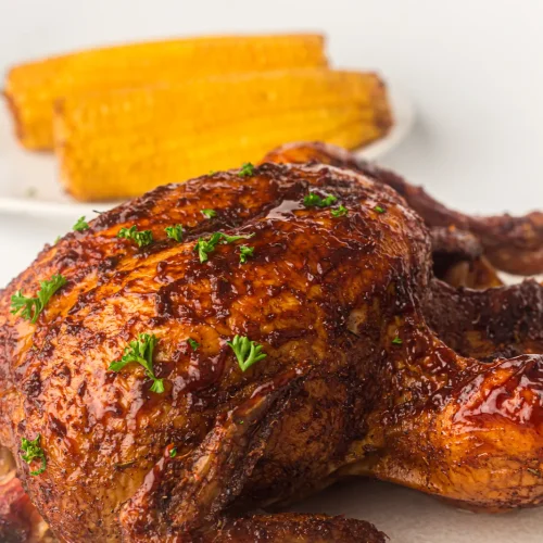 A glazed smoked whole chicken on a plate with grilled corn
