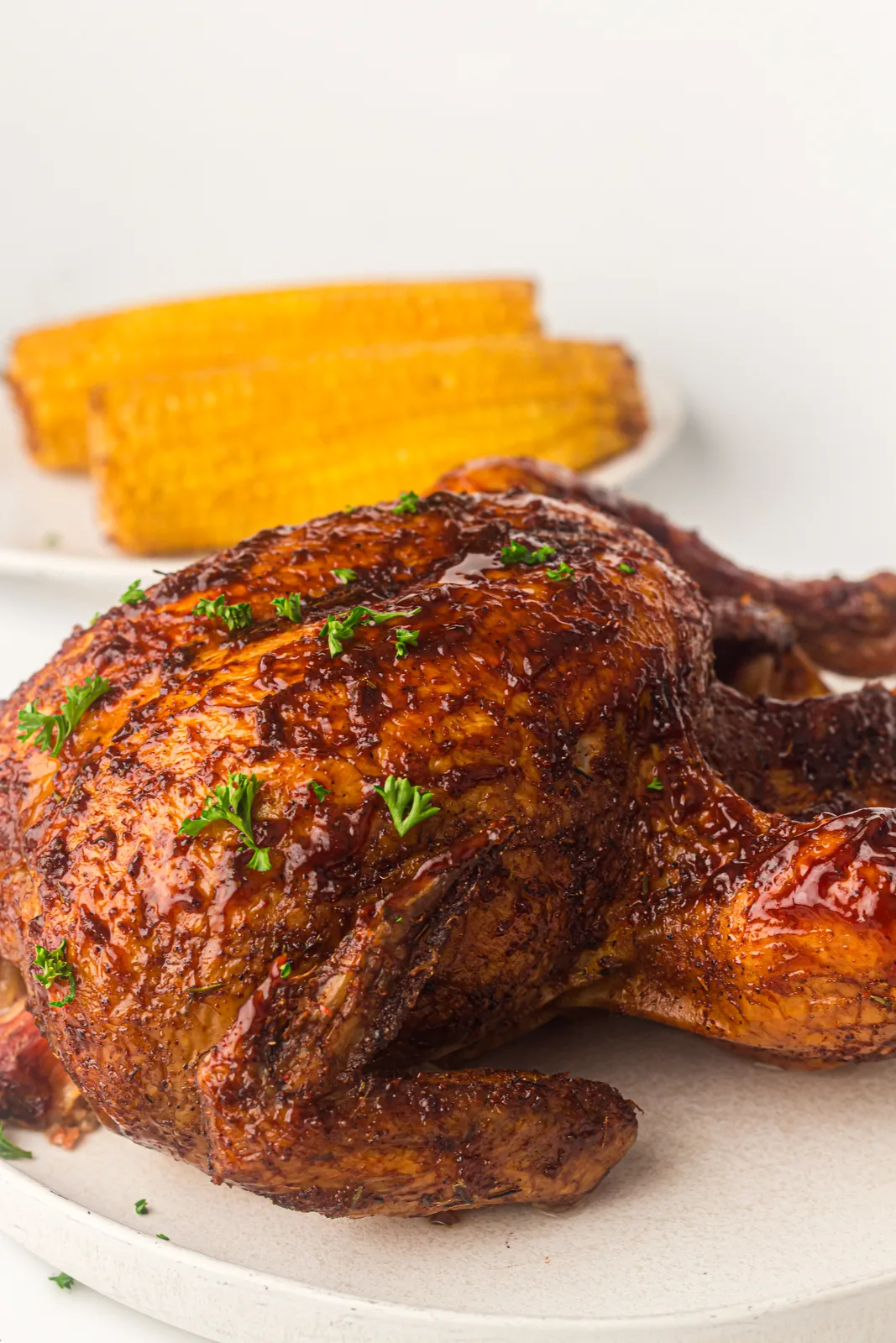 A glazed smoked whole chicken on a plate with grilled corn