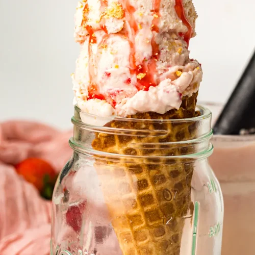 Strawberry cheesecake ice cream on a cone with sauce drizzle
