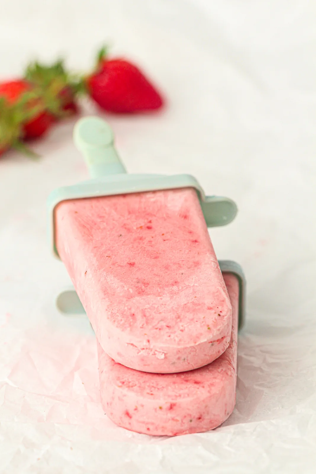 Two creamy strawberry cream popsicles stacked on parchment