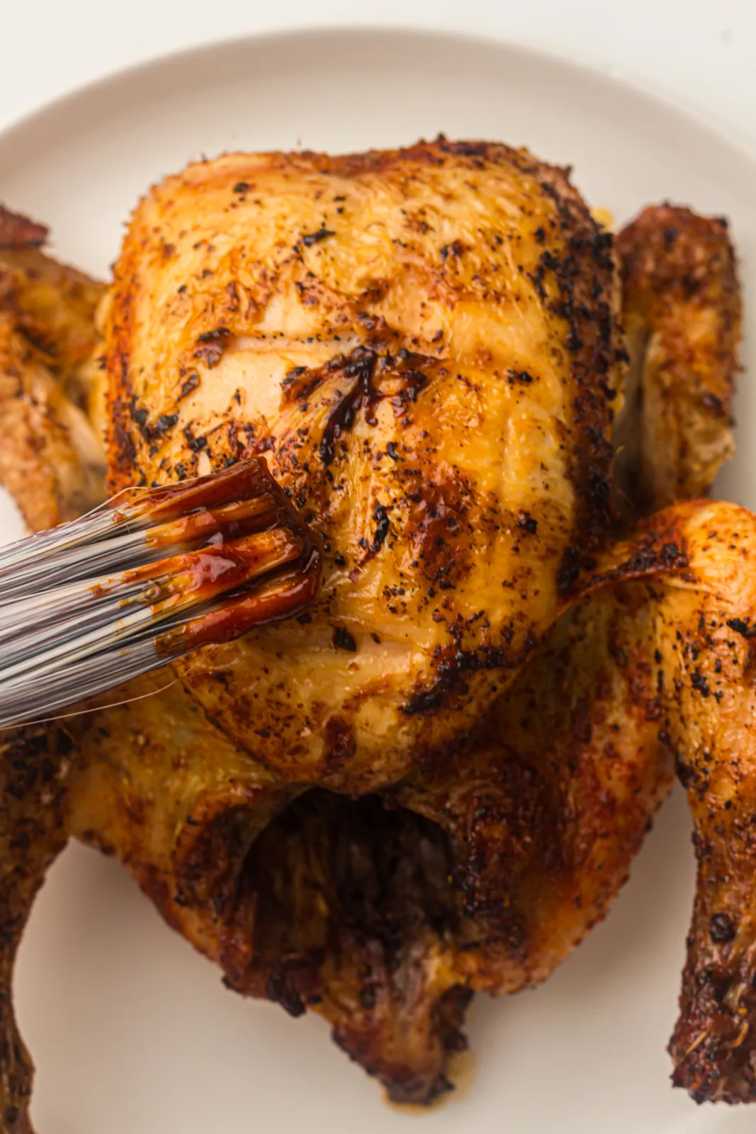 Brushing barbecue sauce over a crispy skinned bird on a plate