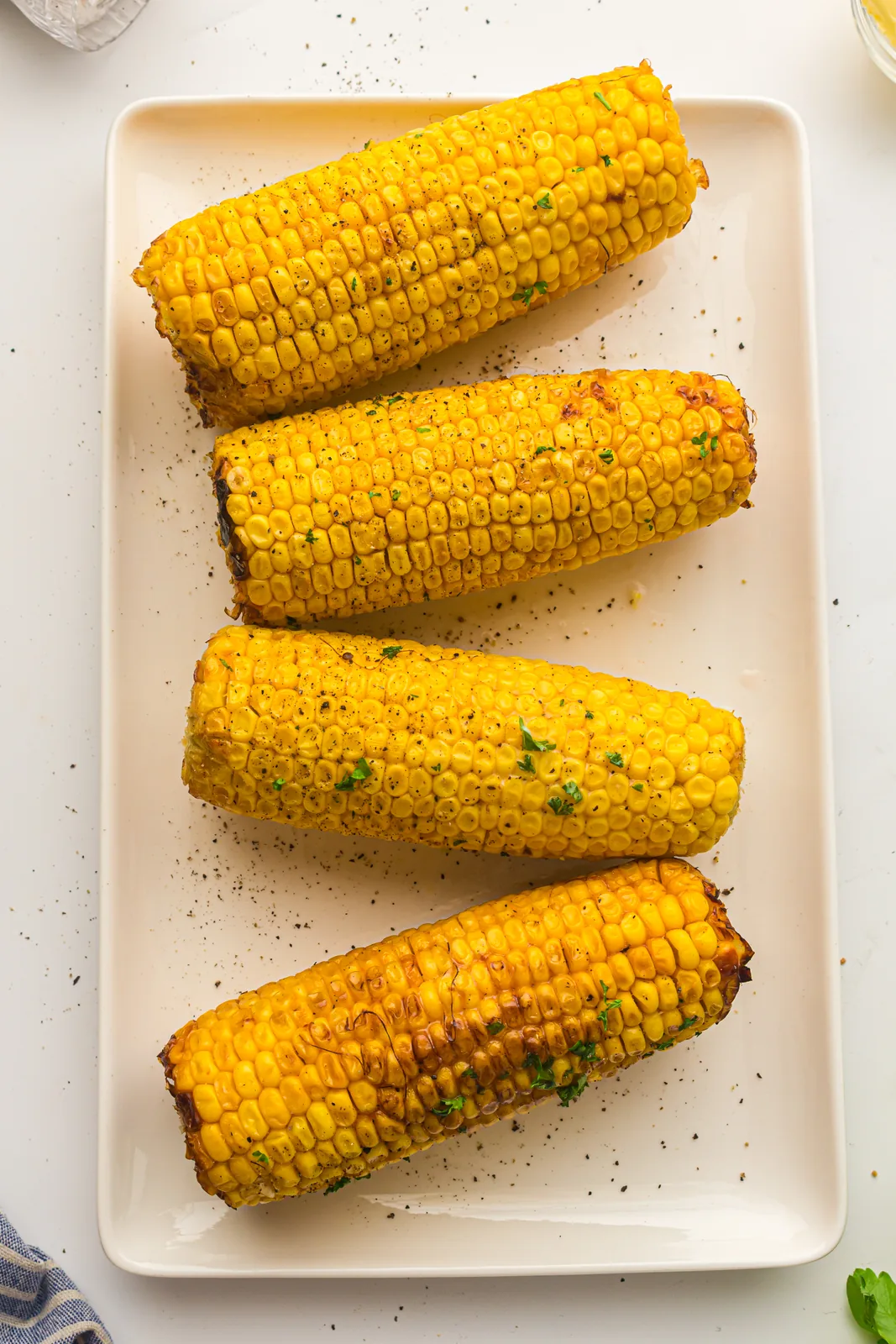 Air fryer corn on the cob served on a long white platter with black pepper and parsley