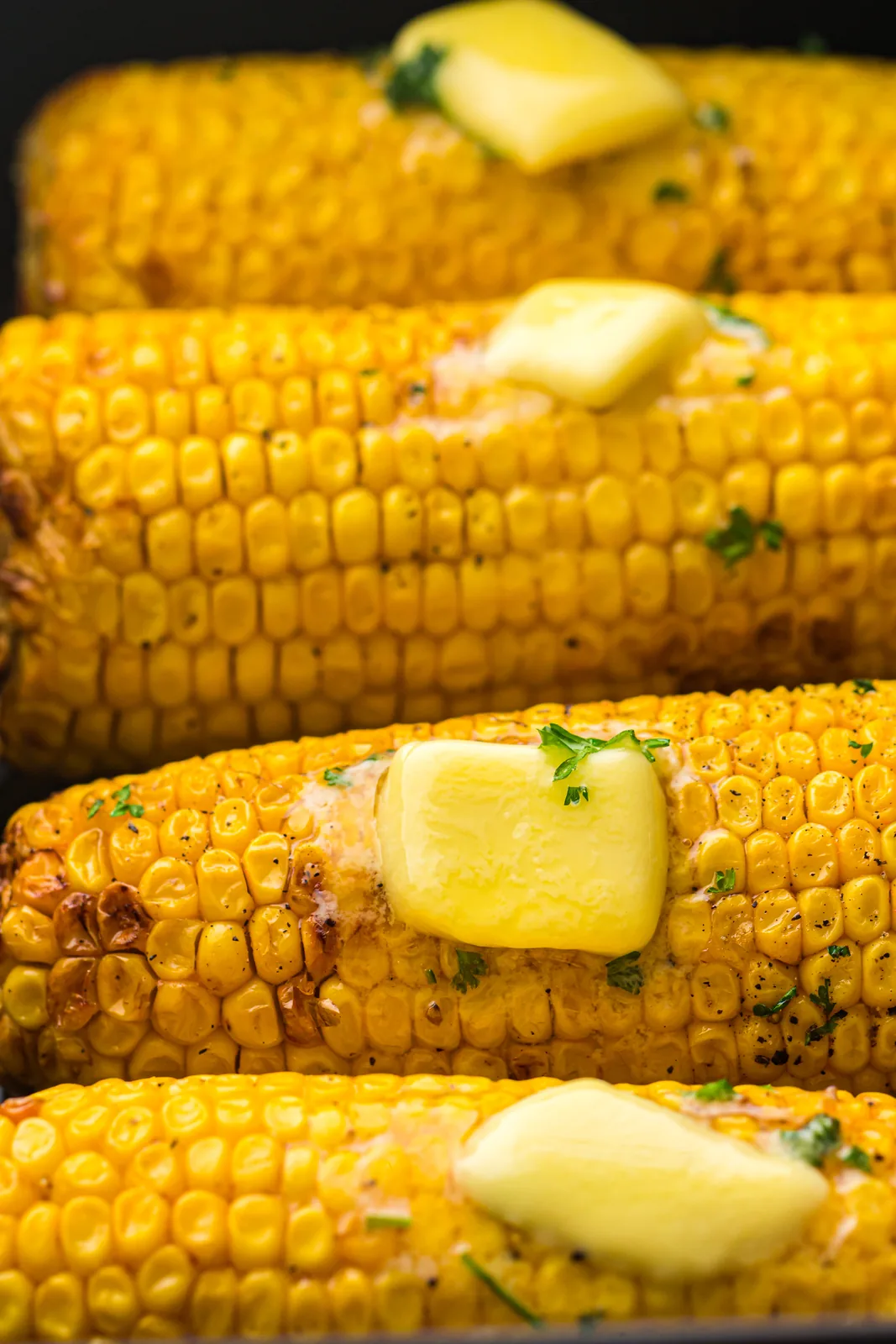 Two golden cobs topped with melting butter pats and chopped parsley