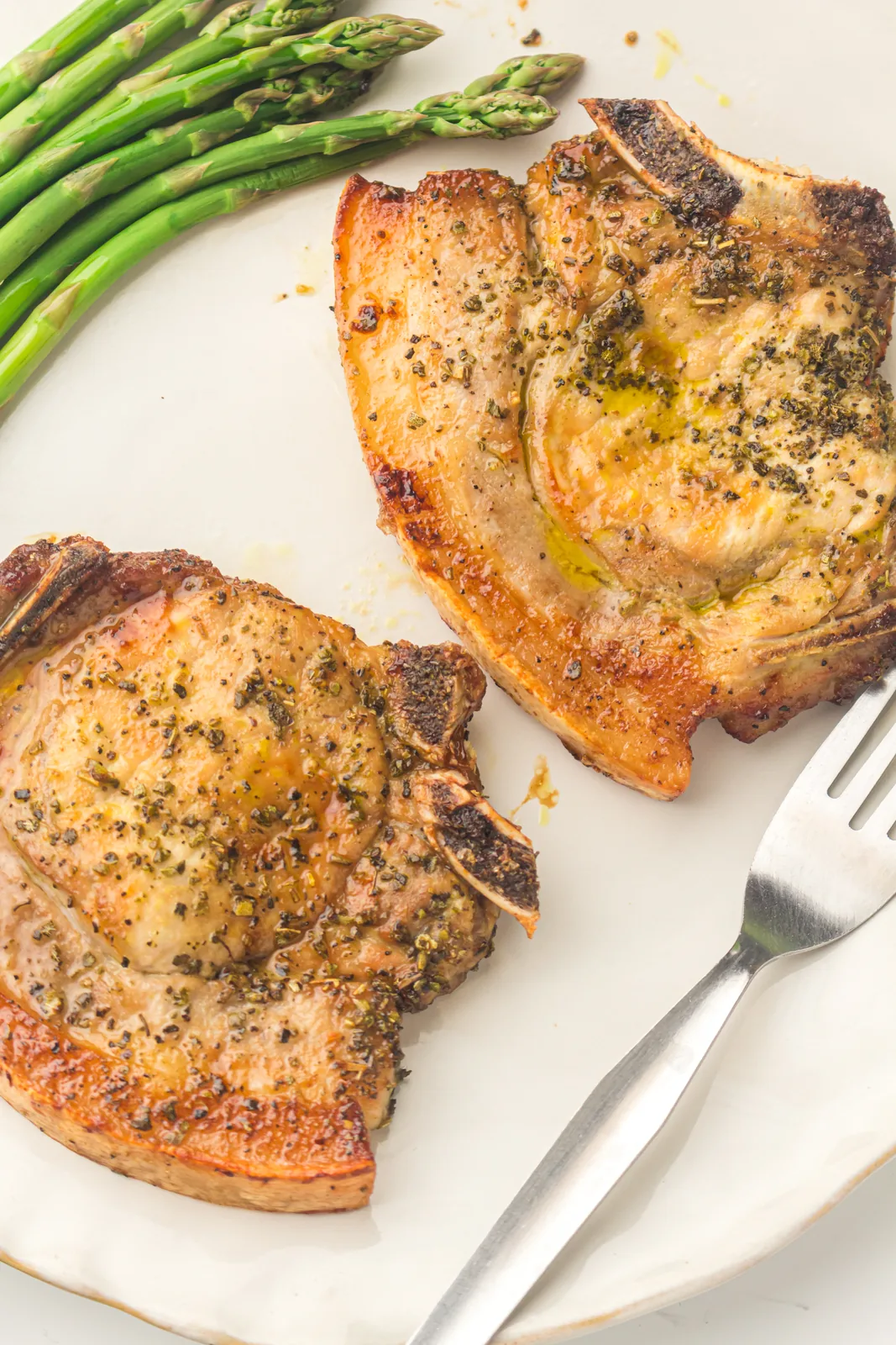 Air fryer pork chops on a white plate with asparagus and a fork