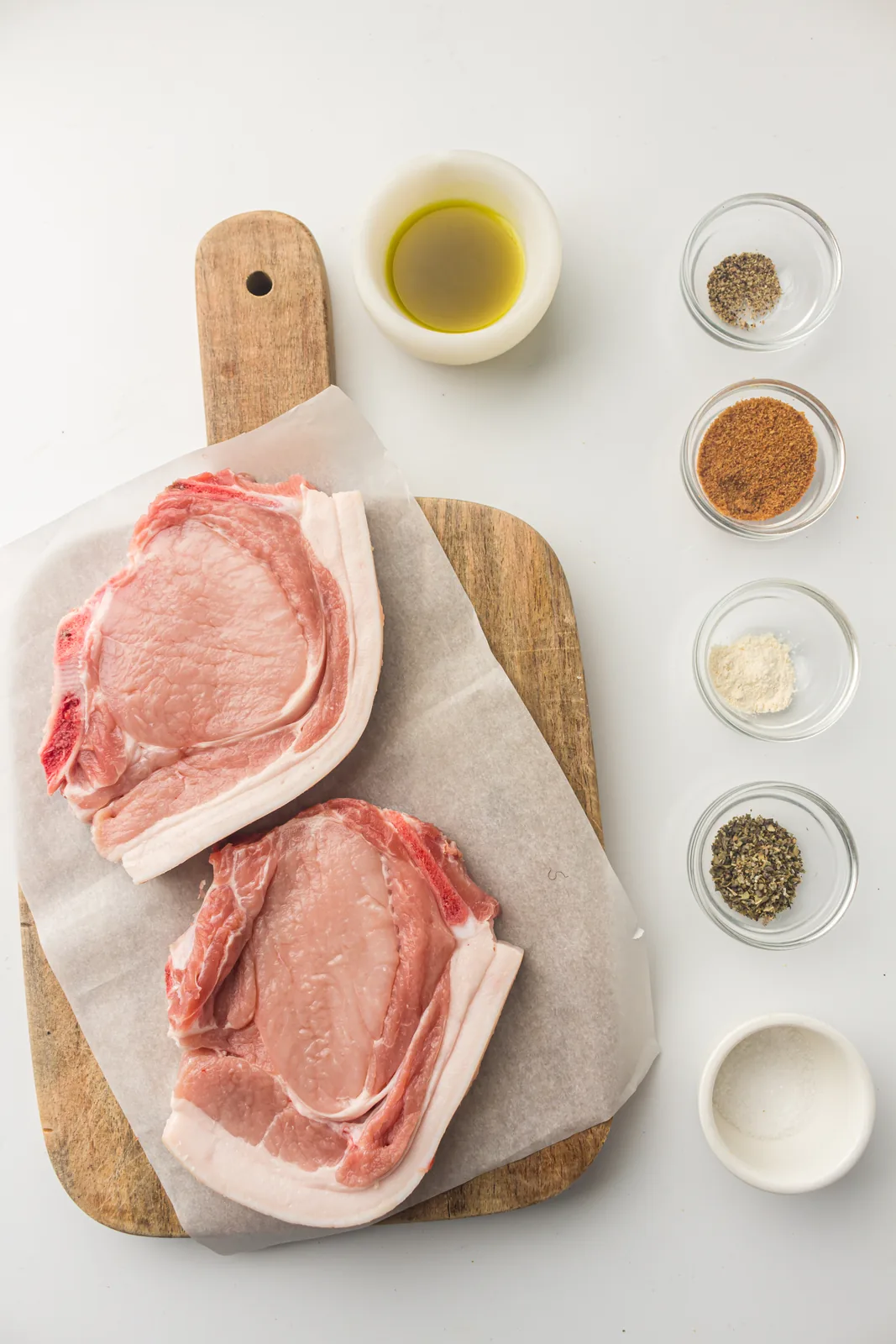Ingredients for air fryer pork chops: two bone-in chops, brown sugar, sage, garlic powder, salt, pepper and oil