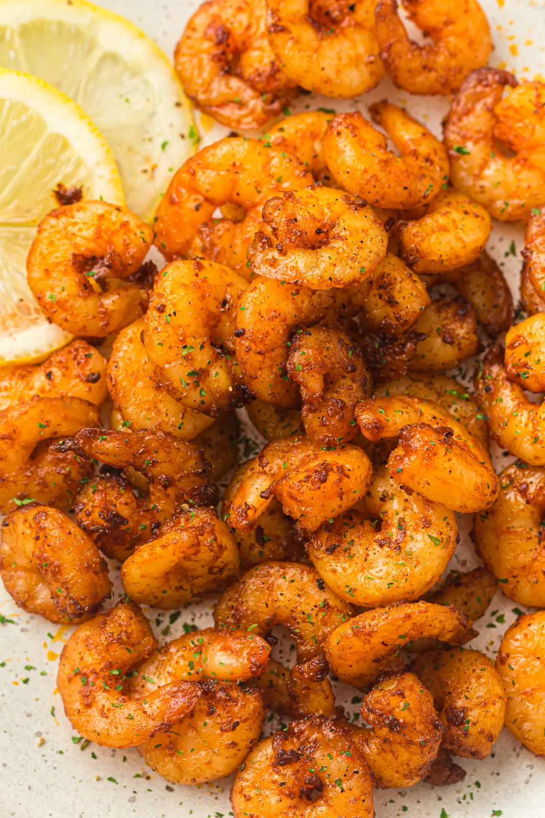 Air fryer shrimp piled on a plate with lemon wedges
