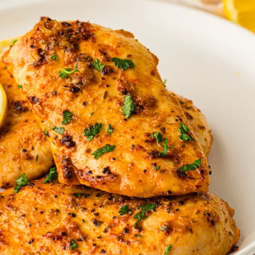 Baked lemon chicken on a white plate with parsley and lemon