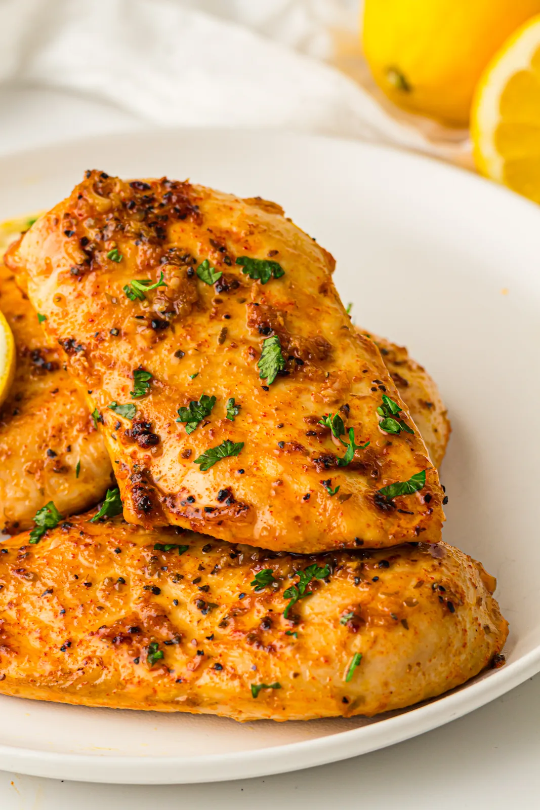 Baked lemon chicken on a white plate with parsley and a wedge of citrus