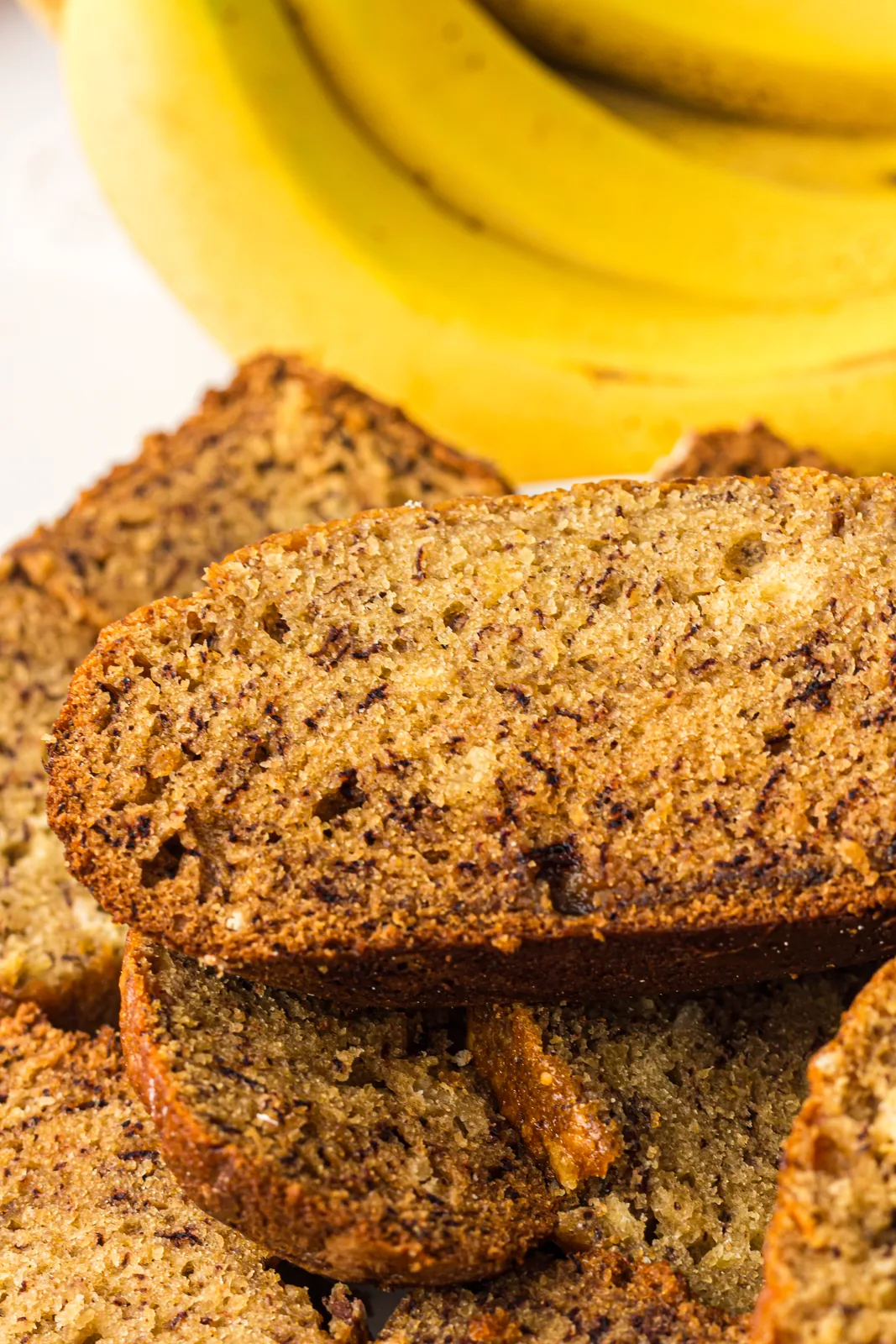Sliced bread machine banana bread stacked beside a bunch of ripe bananas