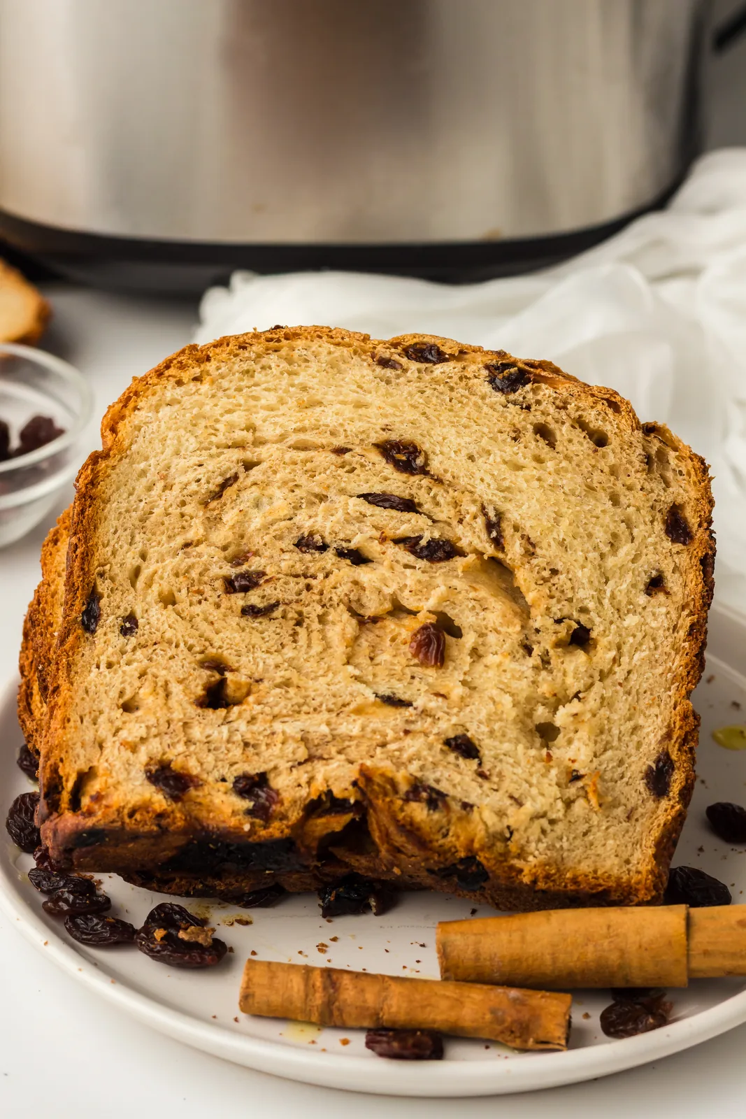 A slice of bread machine cinnamon raisin bread showing the swirl, with cinnamon sticks alongside