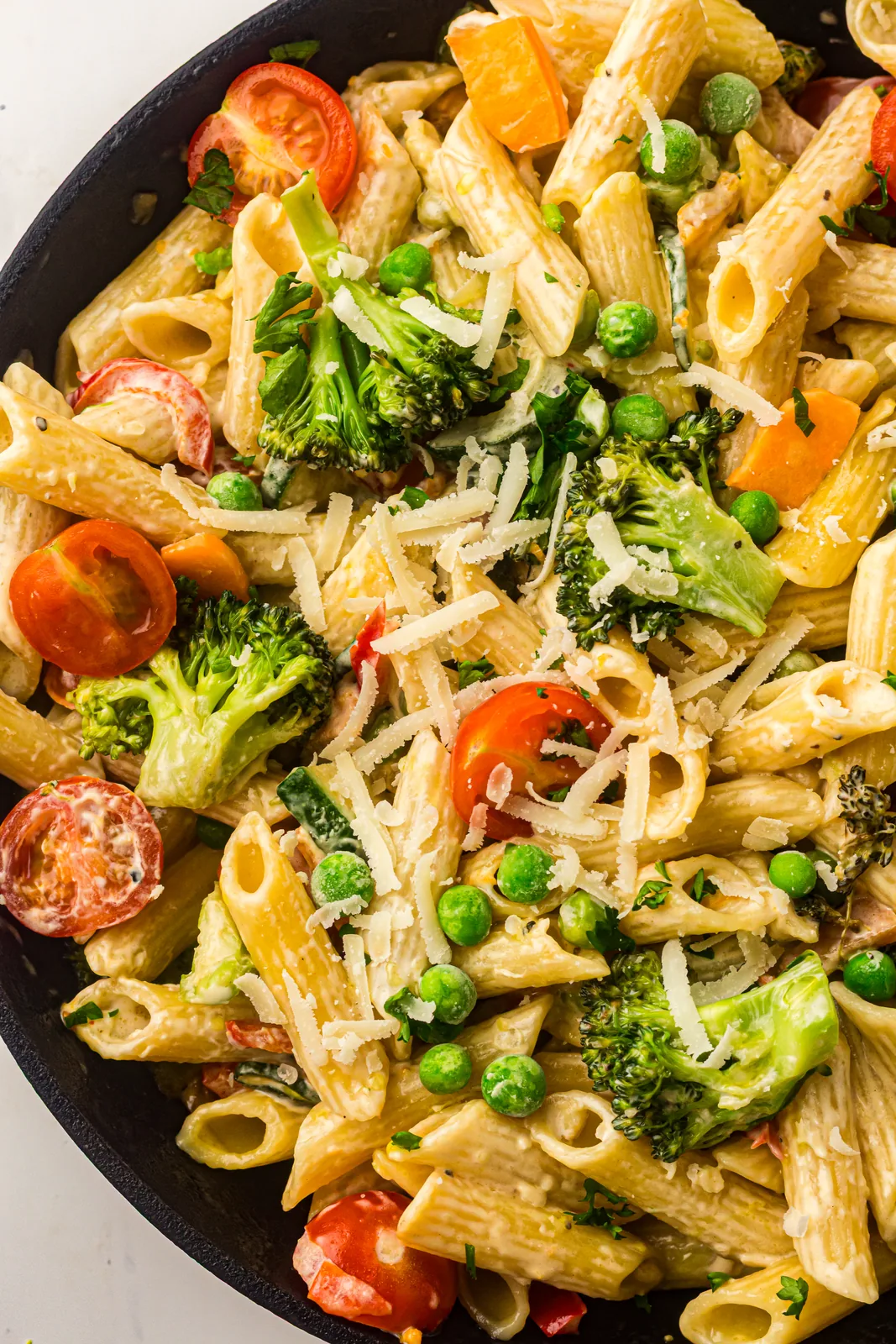 Penne tossed with broccoli, peas and cherry tomatoes in a creamy sauce in a black skillet