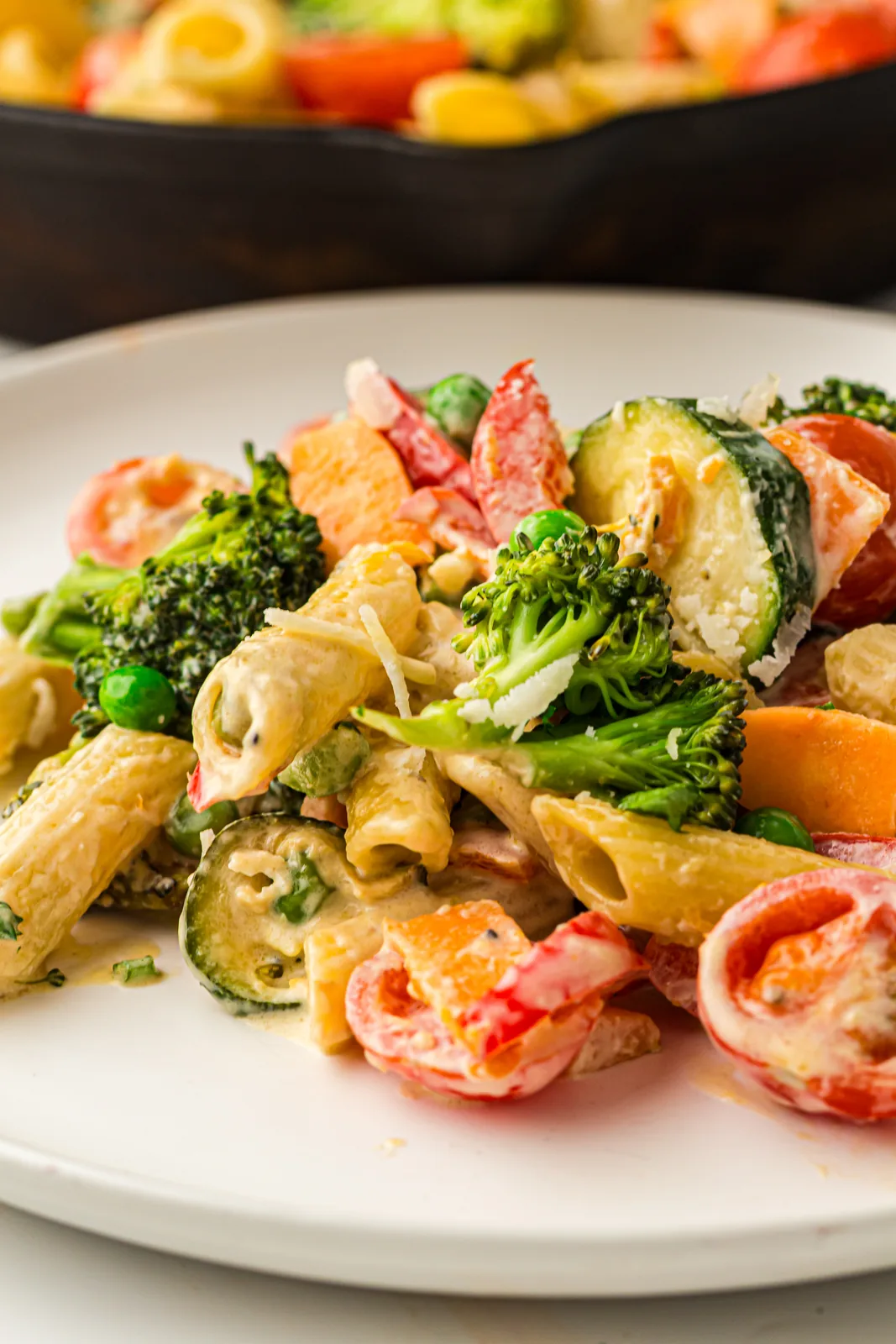 Creamy pasta primavera in a skillet with broccoli, peppers, peas and cherry tomatoes