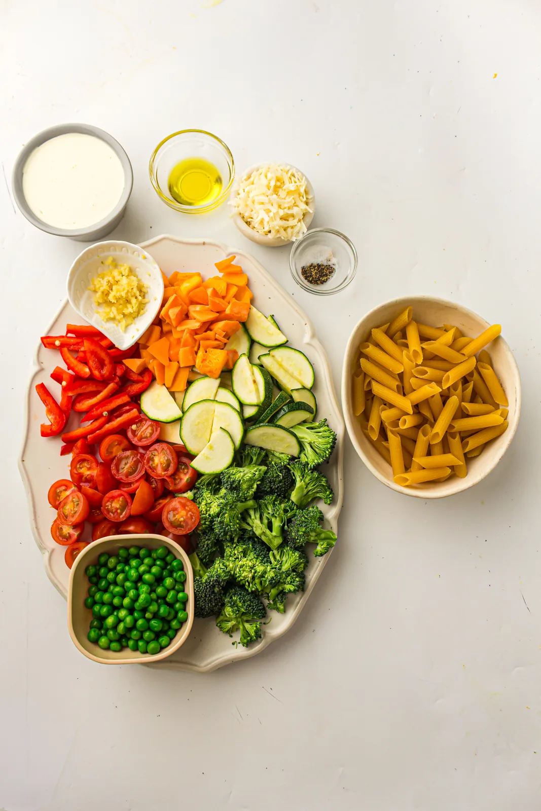Ingredients for pasta primavera: penne, broccoli, bell pepper, courgette, peas, cherry tomatoes, cream and Parmesan