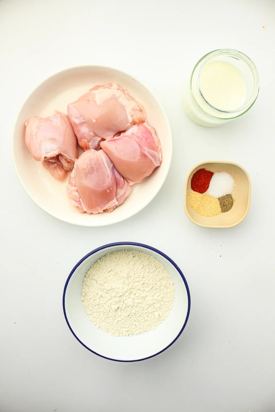 Ingredients for a crispy chicken burger: boneless thighs, milk, seasoned flour and spices