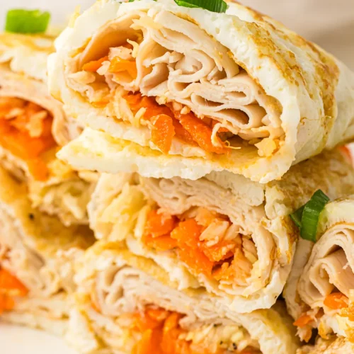 Egg white wraps rolled and halved, stacked on a plate with turkey and carrot inside