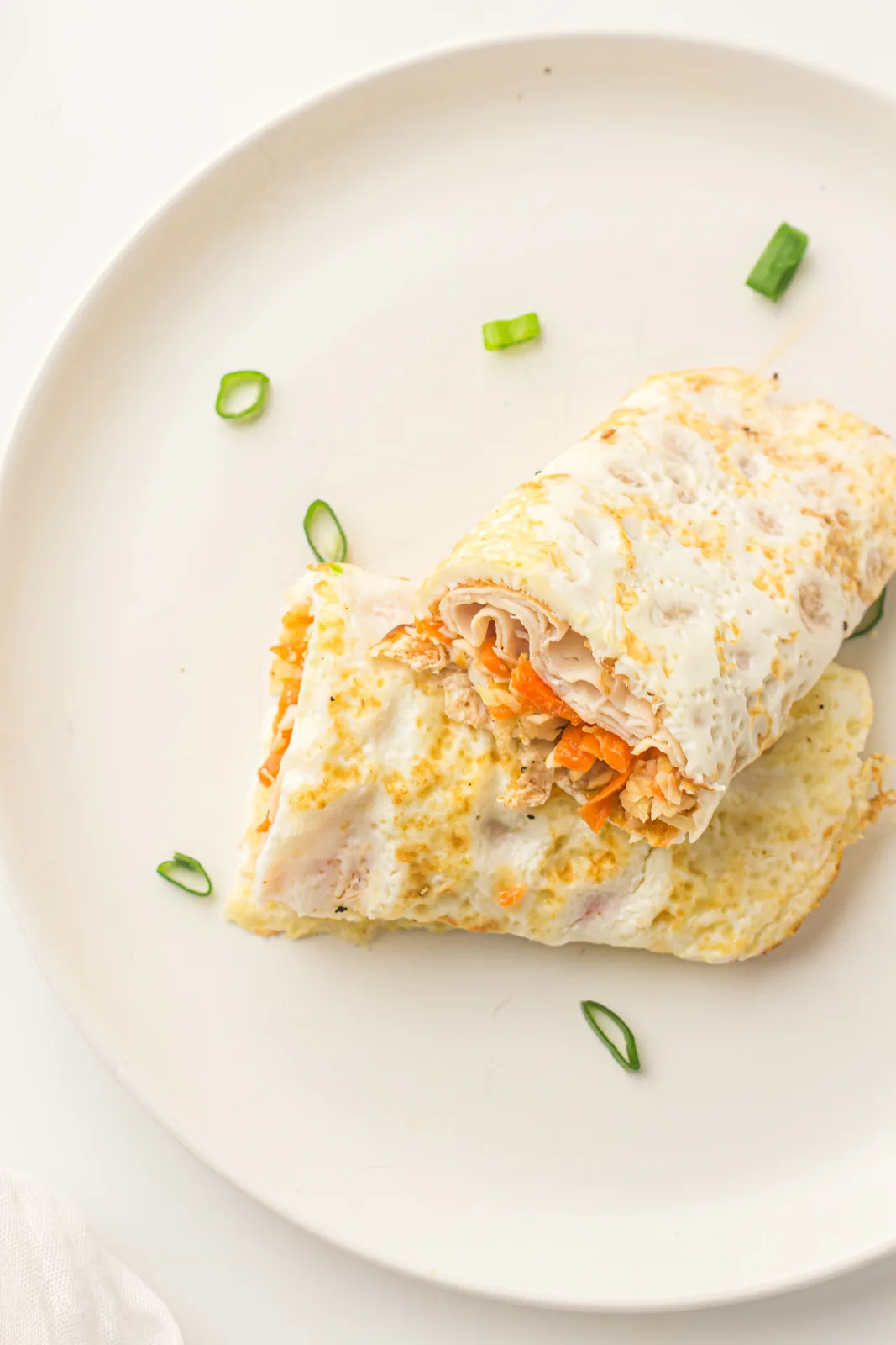 A single pale roll on a white plate with spring onion scattered around it
