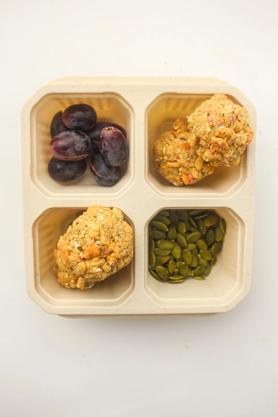 A lunchbox tray packed with two oat bites, grapes and pumpkin seeds