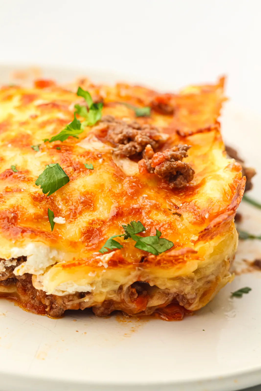 A cut slice on a white plate showing distinct layers of pasta, meat sauce and melted cheese