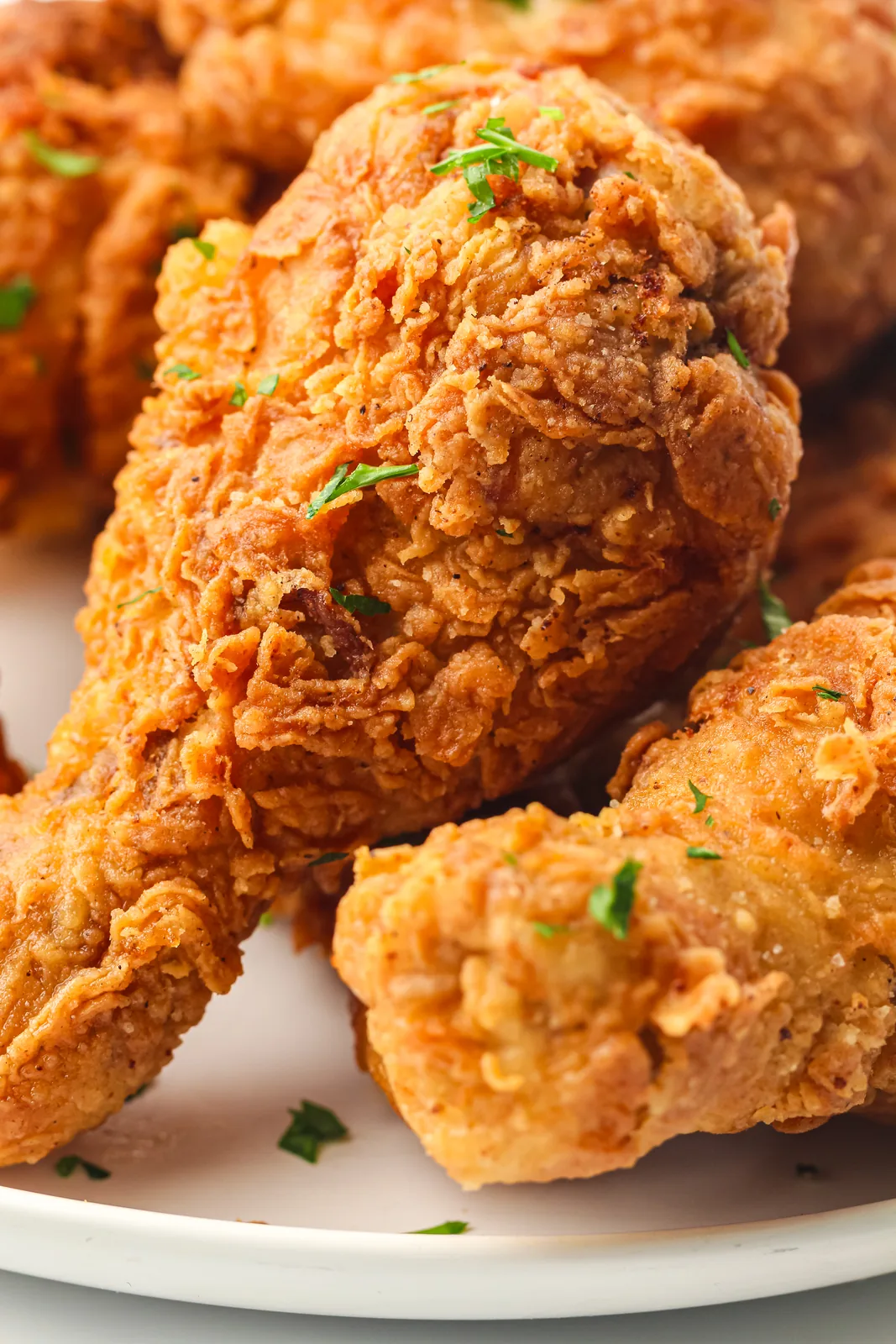 Fried chicken drumsticks piled on a white plate with a craggy golden crust and chopped parsley