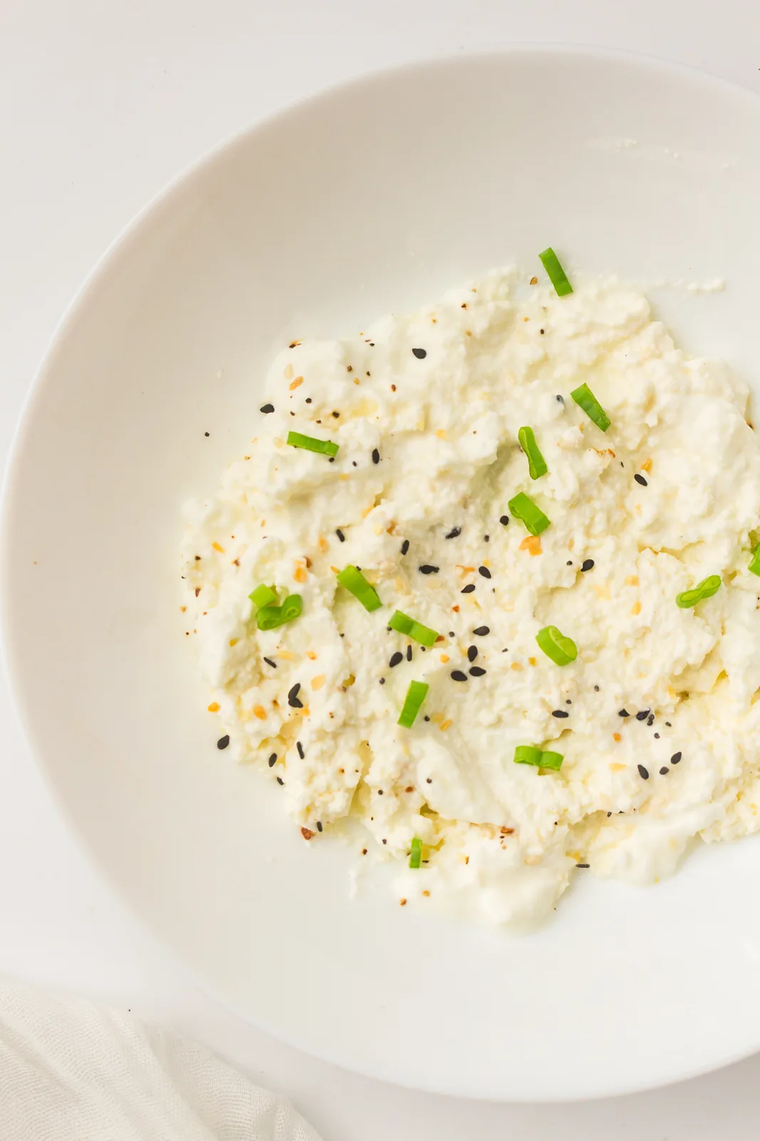 Homemade cottage cheese in a white bowl topped with chives and seeds