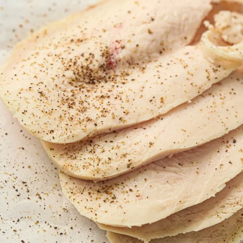 Homemade deli meat sliced thinly and stacked on parchment paper with black pepper